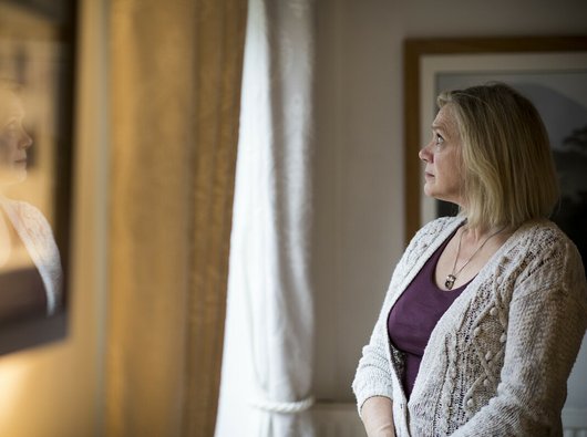 An older woman, at home, looking pensively out of the window.