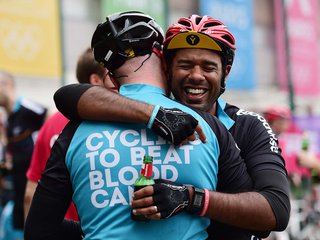 Two cyclists embracing post cycle wearing Blood Cancer UK cycling shirts.