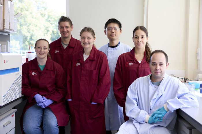 A group of researchers all smiling, wearing Blood Cancer UK lab coats, standing together in the lab.