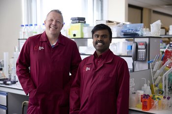 Two researchers wearing Blood Cancer UK lab coats, smiling in a lab.
