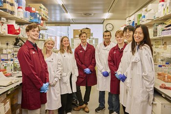 A group of Blood Cancer UK researchers all standing together in a lab, wearing their lab coats and smiling.