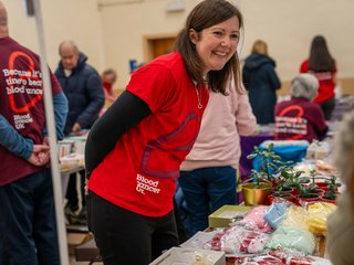 A woman wearing a Blood Cancer UK t-shirt at a fundraiser, smiling.