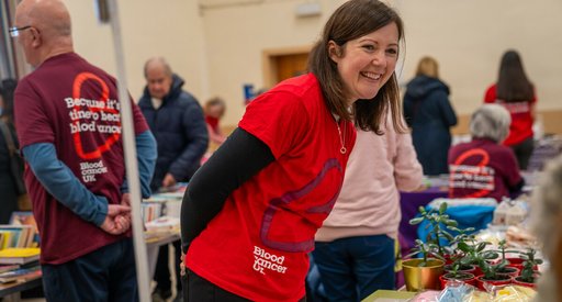 A woman wearing a Blood Cancer UK t-shirt at a fundraiser, smiling.