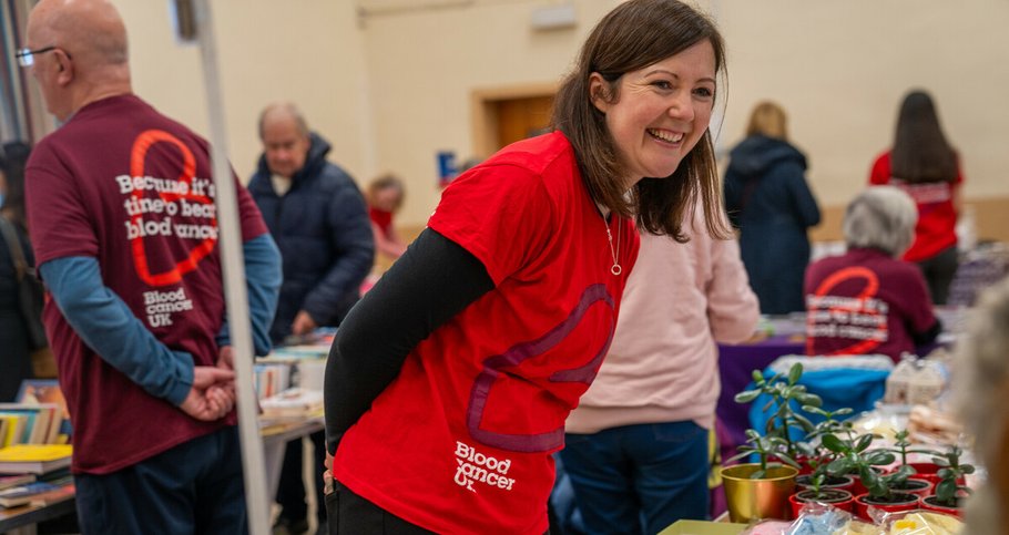 A woman wearing a Blood Cancer UK t-shirt at a fundraiser, smiling.