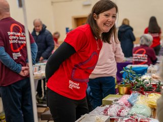 A woman wearing a Blood Cancer UK t-shirt at a fundraiser, smiling.
