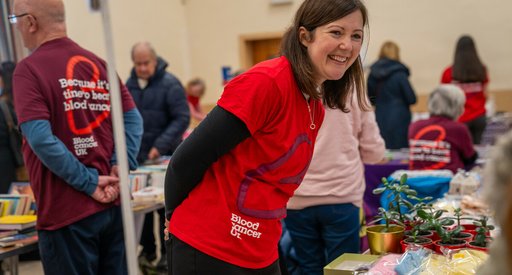 A woman wearing a Blood Cancer UK t-shirt at a fundraiser, smiling.
