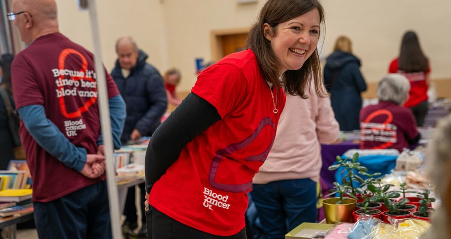 A woman wearing a Blood Cancer UK t-shirt at a fundraiser, smiling.