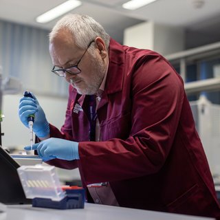 Researcher wearing a branded Blood Cancer UK burgundy lab coat, using equipment in the lab