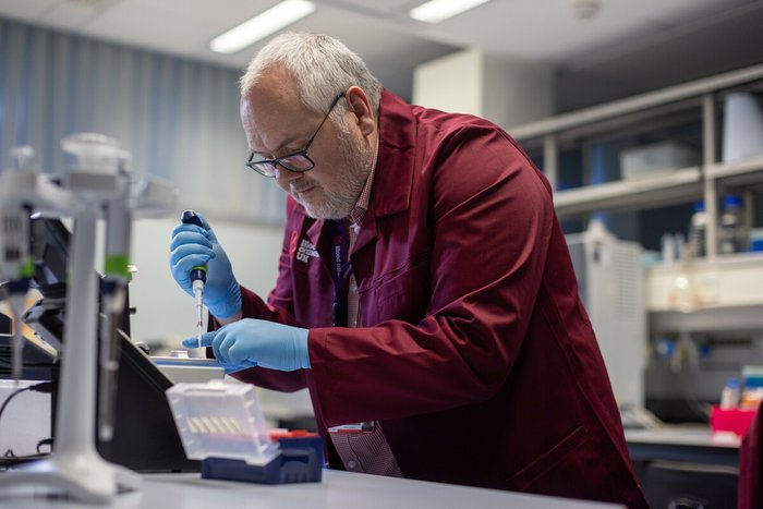 Researcher wearing a branded Blood Cancer UK burgundy lab coat, using equipment in the lab