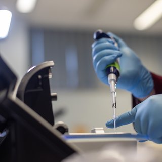 Close up of a researcher's hand and a pipette in the lab.