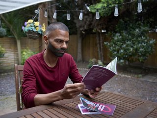 A man sitting in his garden at a table reading a booklet about blood cancer, looking focused but although his thoughts are elsewhere.