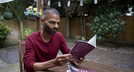 A man sitting in his garden at a table reading a booklet about blood cancer, looking focused but although his thoughts are elsewhere.
