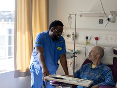 A black healthcare professional giving a caring look to a patient in his hospital bed.