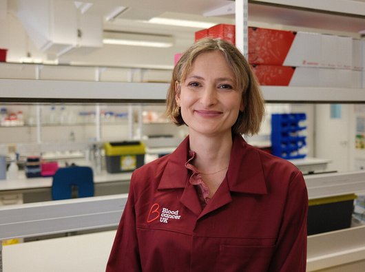 Charlotte Graham, researcher at Kings College London, smiling in her Blood Cancer UK lab coat.