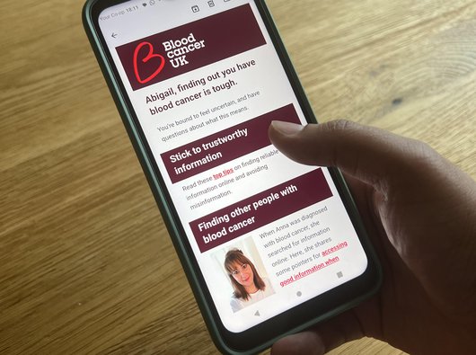 Photo of a hand holding a smart phone, looking at an email that talks about blood cancer information and support.