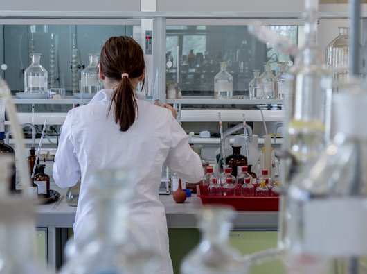 A researcher stands in a laboratory at a work bench surrounded by sample jars