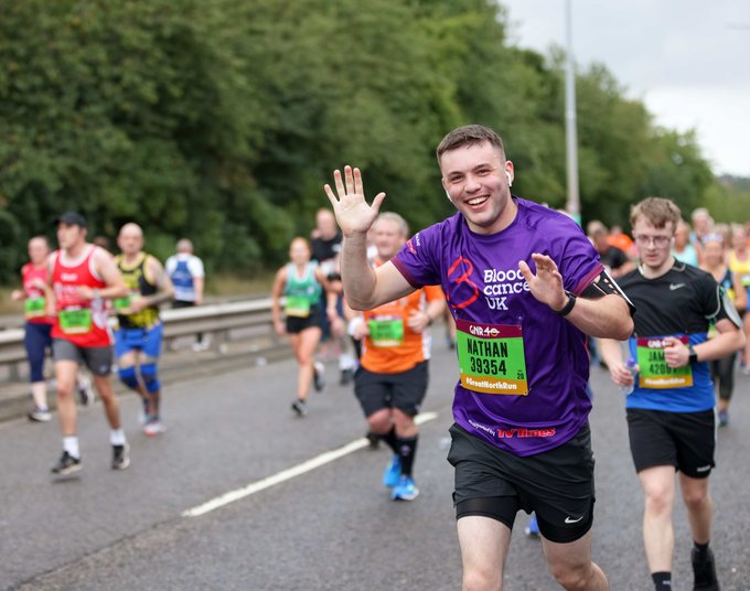 A runner waves at the camera during a marathon; he wears a Blood Cancer UK T-shirt.