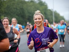 A runner smiles as she runs a marathon; she wear a Blood Cancer UK t shirt.