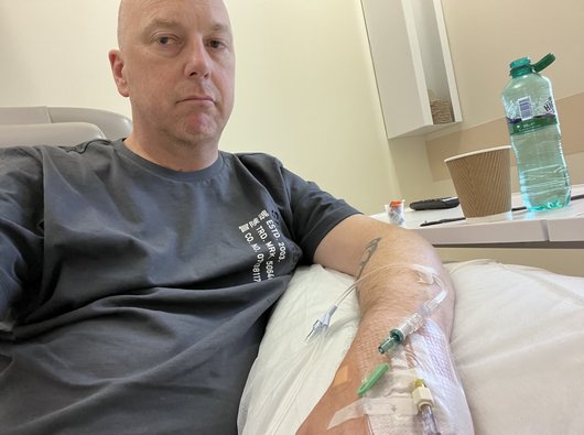Russell is sitting in a hospital bed with a cannula in his arm. He looks tired and unhappy.