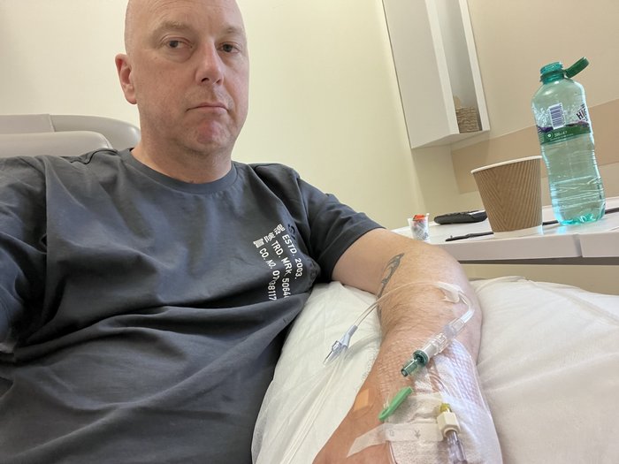 Russell is sitting in a hospital bed with a cannula in his arm. He looks tired and unhappy.