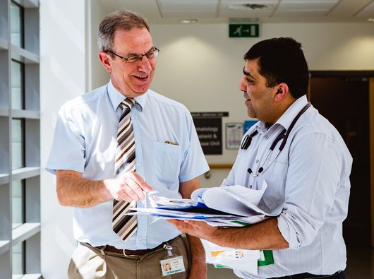 Researcher Professor Peter Hillmen who is funded by Blood Cancer UK talking with a colleague over a booklet of notes.