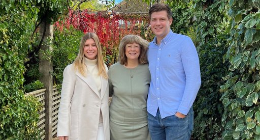 A photo of Samantha Gissel who donates to Blood Cancer UK in memory of her late husband Peter. She is standing in a garden with her children either side of her.