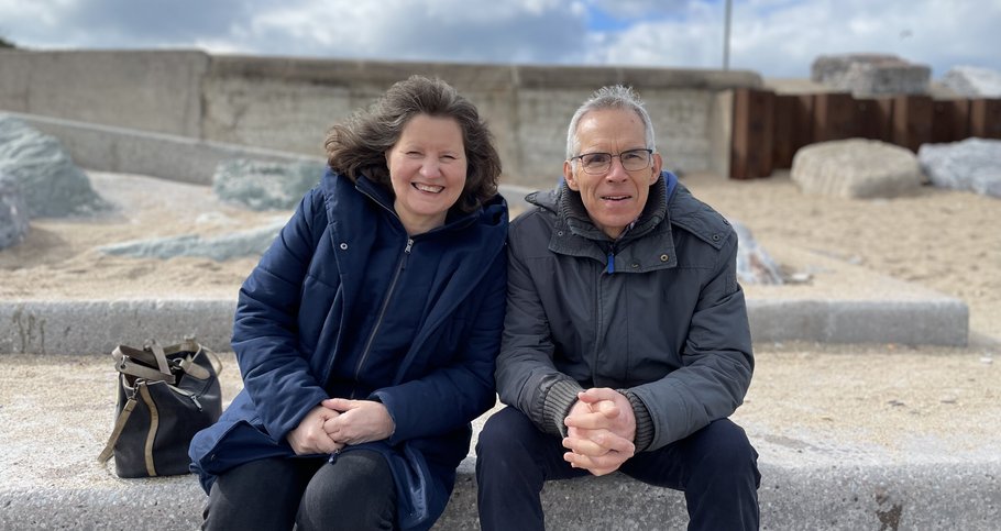 Sarah's mum and dad sitting on a wall outside, smiling.