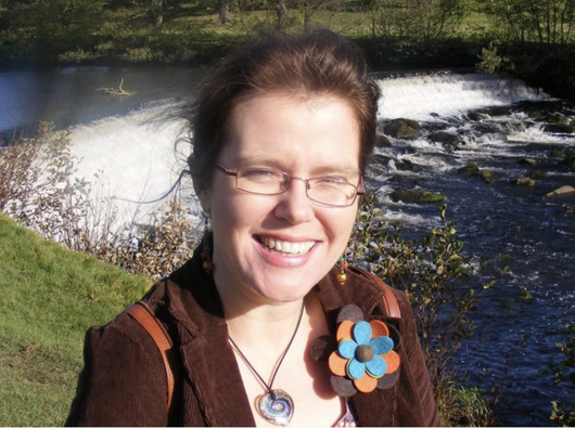 Joanna, who was diagnosed with chronic myeloid leukaemia (CML), standing beside a river smiling at the camera.
