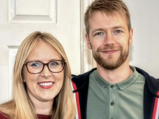 Emma, who was diagnosed with acute lymphoblastic leukaemia (ALL), smiling next to her partner in front of a wooden door.