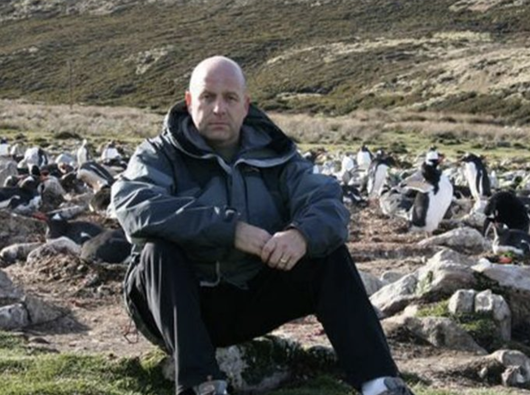 Edward, a retired soldier who was diagnosed with myeloma, sitting on a rock on a hiking trail looking straight faced at the camera.