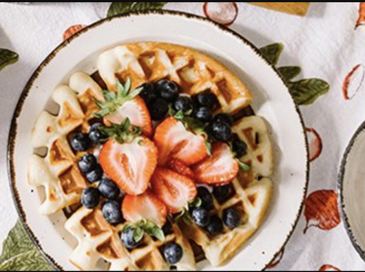 Close-up of a tablescape with a plate of waffles topped with fresh blueberries and strawberries