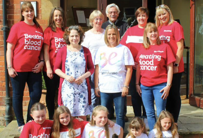 A group of women of various ages and generations - plus one man - poses together against a house in a backgarden.