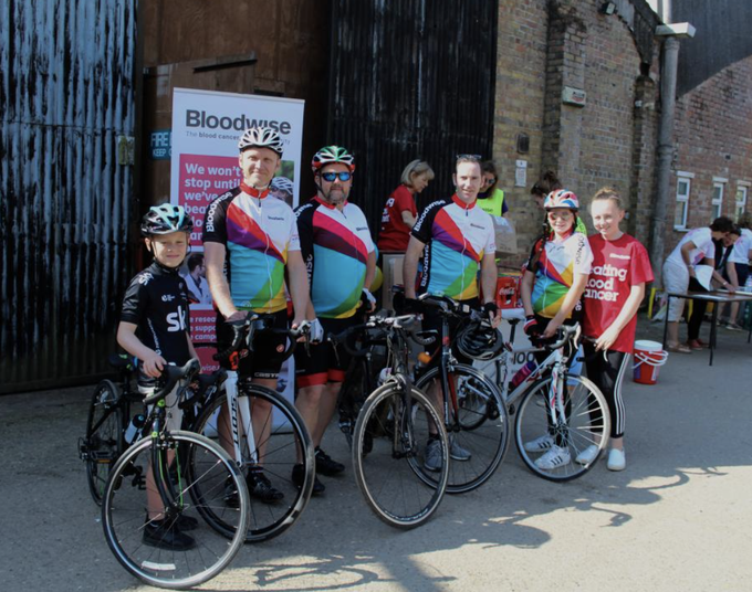 A group of riders of various ages pose together with their bicycles at a Bloodwise cycling event.