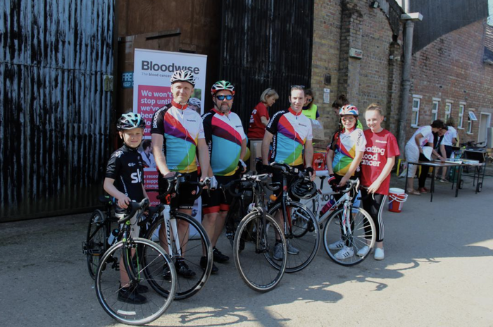 A group of riders of various ages pose together with their bicycles at a Bloodwise cycling event.