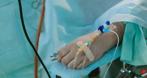 Close up of the hand of someone lying in a hospital bed with a cannula inserted.