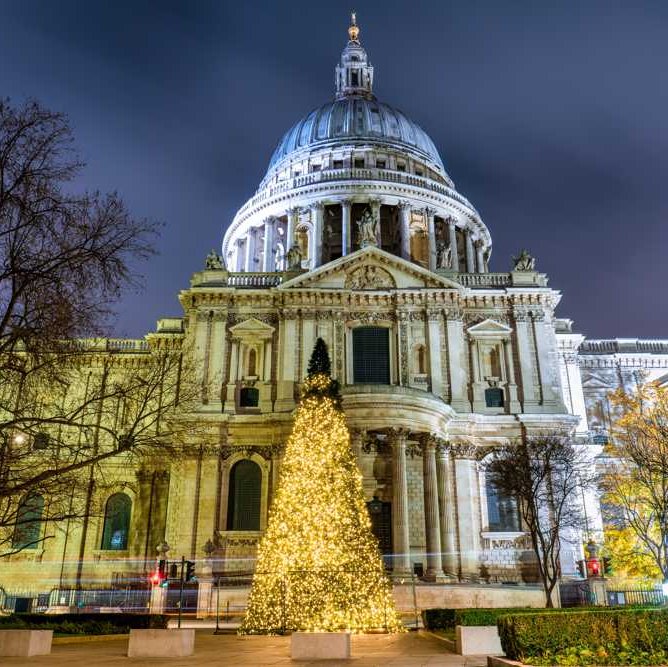 St Paul's Cathedral, London lit up at night with Christmas tree in front.