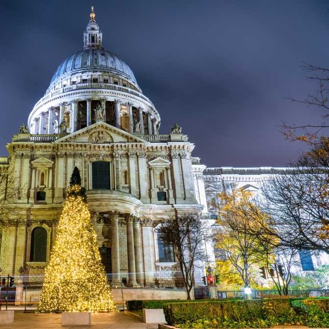 St Paul's Cathedral, London lit up at night with Christmas tree in front.