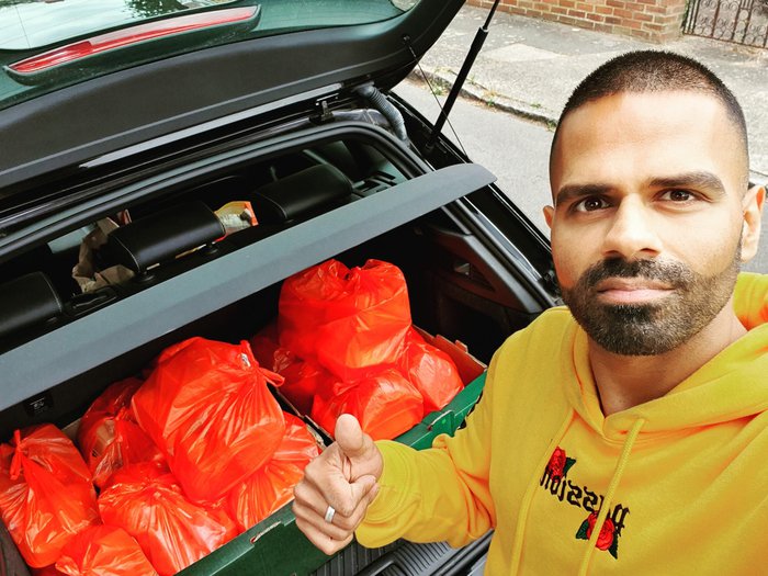 Sunny, who was diagnosed with stage four non-Hodgkin lymphoma, standing in front of a car boot filled with orange plastic bags of hot food that gets delivered to local  charities.