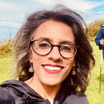 Profile photo of psychotherapist Surabhi, who is outside in the sun, wearing glasses and smiling.