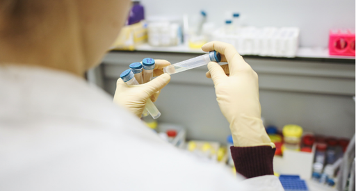 Back shot of a researcher in a lab looking closely at test tubes in their hand.