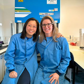 Two women in blue lab coats sitting and smiling