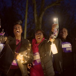 Four people taking part in the charity walk 'Walk of Light', holding up lanterns and wrapped in fairy lights.