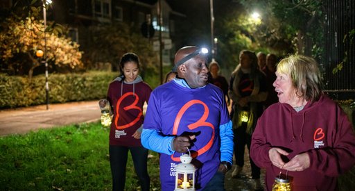 A group of people walk together at twilight, carrying lanterns and wearing Blood Cancer UK t-shirts