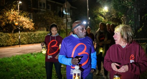 A group of people walk together at twilight, carrying lanterns and wearing Blood Cancer UK t-shirts