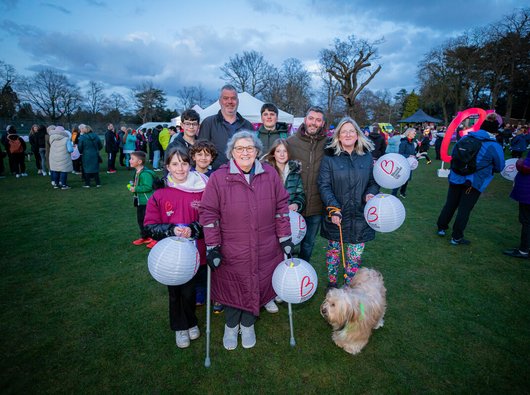 Kath and her family all standing under a twilight sky, carrying lanterns and smiling, about to embark on their walk of light.