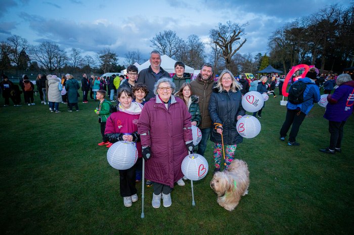 Kath and her family all standing under a twilight sky, carrying lanterns and smiling, about to embark on their walk of light.