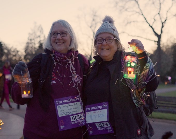 Two people smiling at the camera at Walk of Light Birmingham, showing off their Blood Cancer UK merch.