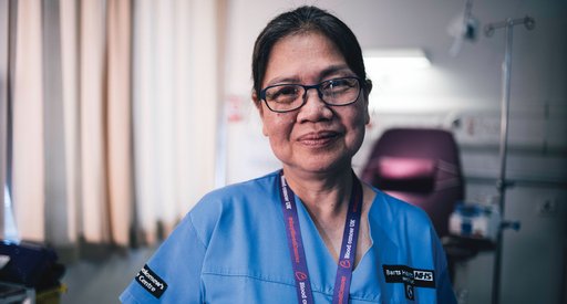 A close-up vignette of a healthcare professional, smiling at the camera wearing blue scrubs.