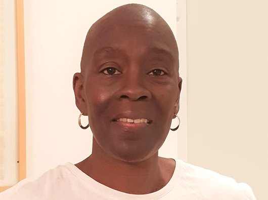 Photo of Yvonne who is bald. She is wearing hoop earrings and looking into the camera smiling.