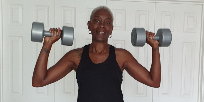 Yvonne, who was diagnosed with acute myeloid leukaemia (AML), shoulder pressing two grey dumbbells whilst smiling at the camera.